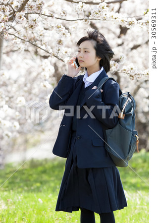 制服を着て桜の木の前に立つ女子高生の写真素材