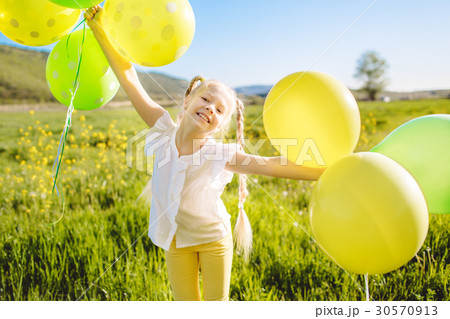 Little happy girl with green and yellow balloons 30570913
