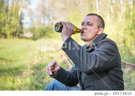 Man sitting on the rails drinking beer 30573610