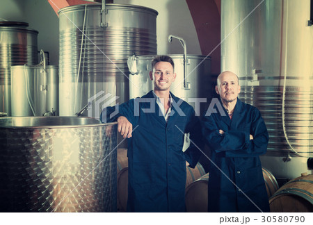 Two happy men in uniforms standing in winery fermentation compartment Two happy men in uniforms standing in winery fermentation compartment 30580790