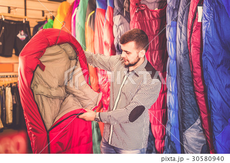 Young male customer choosing new sleeping bag Young male customer choosing new sleeping bag 30580940