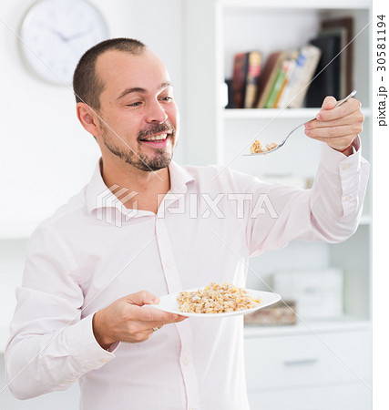 Positive young man eating porridge Positive young man eating porridge 30581194