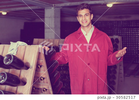 Man winery working in aging section with bottle racks in cellar Man winery working in aging section with bottle racks in cellar 30582517