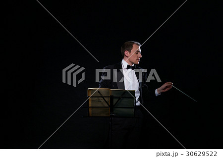 Orchestra conductor in black tuxedo in dark studio 30629522