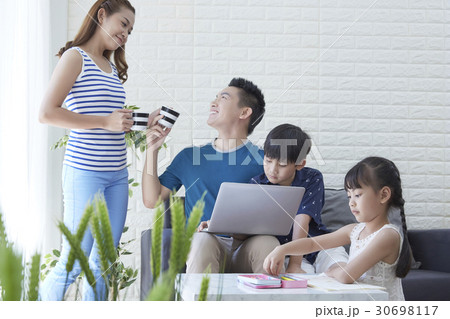 Dad is taking a cup from mom and kids are studying. 30698117
