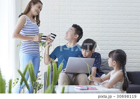 Dad is taking a cup from mom and kids are doing homework. 30698119
