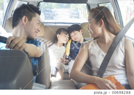 a family of parents smiling and two children sleeping on a car 30698288