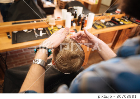 Pleasant professional hairdresser working with his Pleasant professional hairdresser working with his 30703981