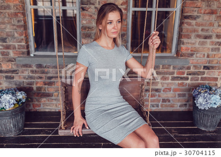 Beautiful blonde woman in gray dress sitting on a 30704115
