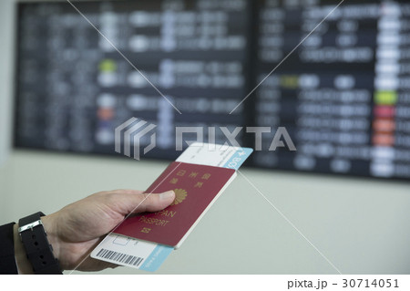 パスポートを持って電光掲示板を見るビジネスマン手元の写真素材