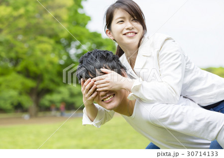 公園カップルイメージ 彼女を背中におんぶする 彼女は目隠しするの写真素材