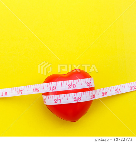 Red heart shape and white measurement tape on yellow background. For heart check up or checking size concept Red heart shape and white measurement tape on yellow background. For heart check up or checking size concept 30722772