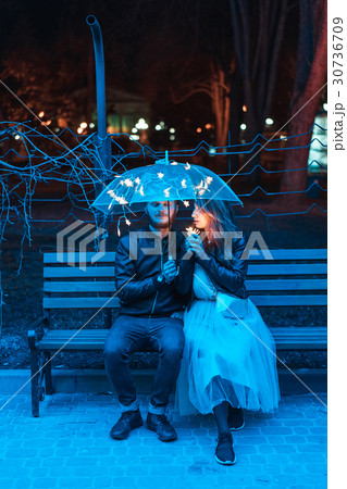 Guy and girl sitting on a bench under an umbrella 30736709