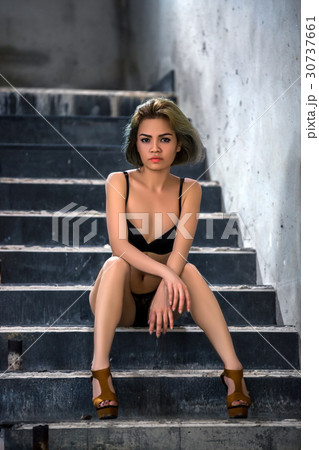 Young woman wearing bikini top and hot pants sitting on stairs looking up  stock photo - OFFSET