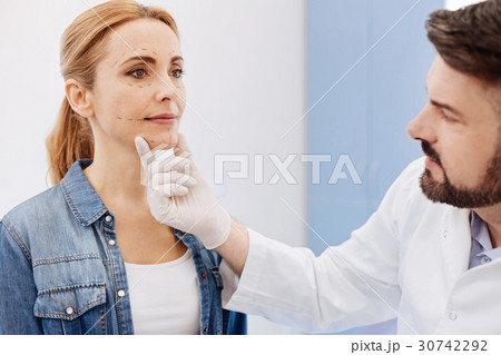 Serious cosmetic surgeon holding his patients chin 30742292