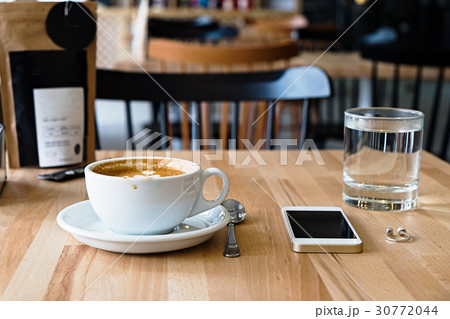White mug of cappuccino and phone on wooden table 30772044