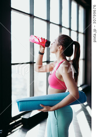 Young woman drink water and hold rubber mat in gym Young woman drink water and hold rubber mat in gym 30799676