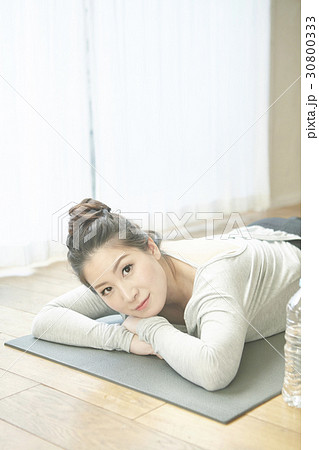 A woman is lying down to relax after doing yoga exercise. 30800333