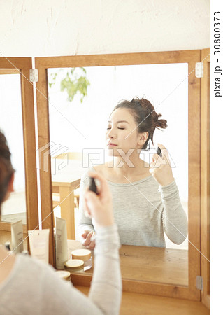 The woman is spraying mineral water on her face at home. 30800373