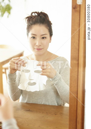 A woman is applying facial mask sheet and looking in the mirror. A woman is applying facial mask sheet and looking in the mirror. 30800380