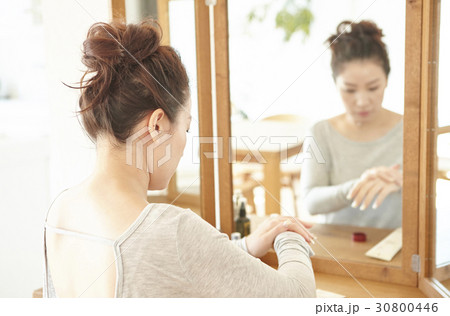 a woman applies moisturizer on her hands in front of a mirror. 30800446