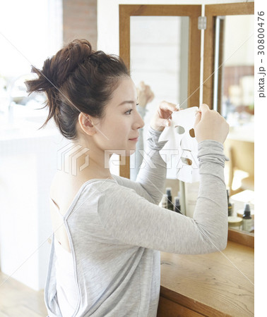 The woman is holding a facial mask sheet in front of a mirror 30800476