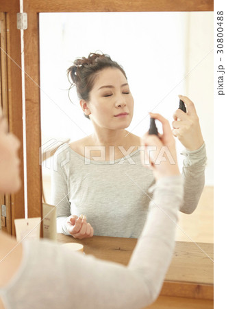 a woman is spraying lotion on her face at home. 30800488