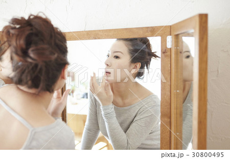 a woman looks at a mirror and touches her lips. 30800495