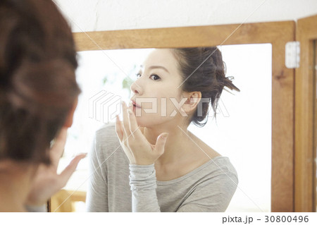 a woman is looking at a mirror and touching her lips. 30800496