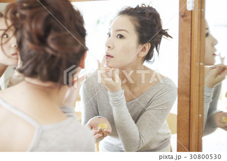 a woman is in front of a mirror and applies cream on her lips. a woman is in front of a mirror and applies cream on her lips. 30800530