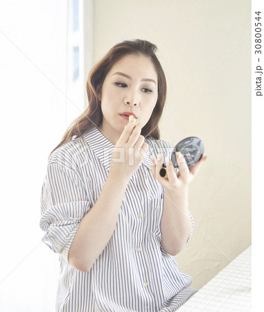 a woman looks at a small mirror and makes up by lipstick. 30800544