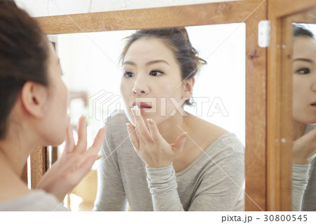 a woman is looking at a mirror and touching her lips. 30800545