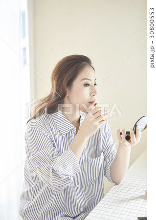 a woman holds a small mirror and makes up by lipstick. a woman holds a small mirror and makes up by lipstick. 30800553
