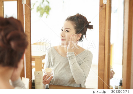 a woman is applying cream on her cheek at home. 30800572