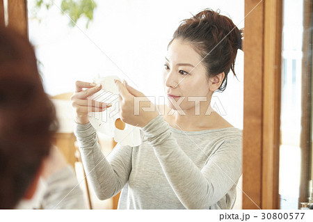 a woman lifts and looks at facial mask sheet before applying. 30800577