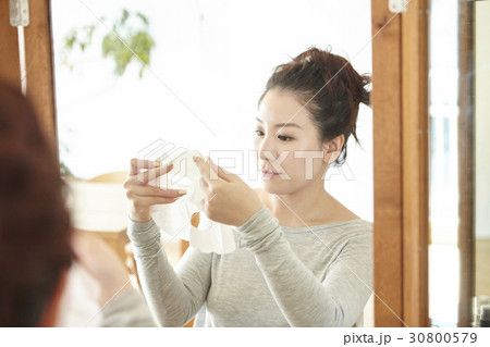 a woman lifts up and looks at facial mask sheet before applying. a woman lifts up and looks at facial mask sheet before applying. 30800579
