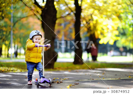 Toddler boy in safety helmet learning to ride scooter Toddler boy in safety helmet learning to ride scooter 30874952