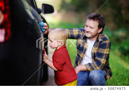 Middle age father with his toddler son washing car together outdoors Middle age father with his toddler son washing car together outdoors 30874975
