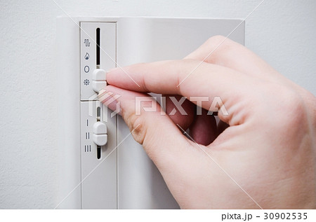 Hand switches air conditioner thermostat on wall 30902535