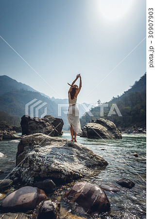 Woman make yoga pose on a bank of Ganga river Woman make yoga pose on a bank of Ganga river 30907903