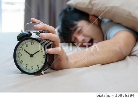 Sleepy man in bed  extending hand to alarm cock 30956294