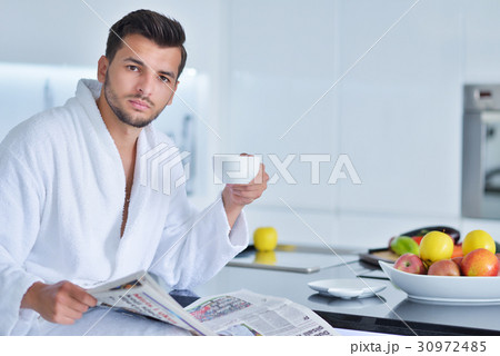 Young man in bathrobe sitting on kitchen worktop Young man in bathrobe sitting on kitchen worktop 30972485