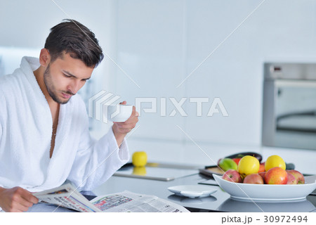 Young man in bathrobe sitting on kitchen worktop 30972494