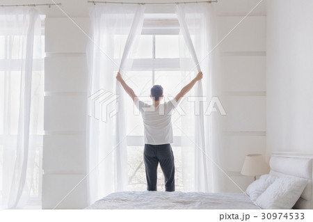 Young man opening window curtains 30974533