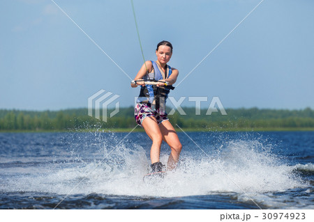 slim woman riding wakeboard on wave of boat 30974923