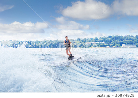 slim woman riding wakeboard on wave of boat 30974929