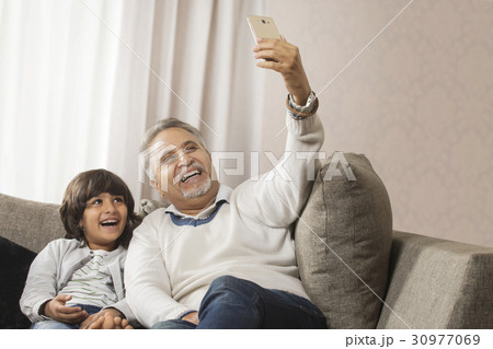 Happy grandfather and grandson taking a selfie together sitting on sofa 30977069