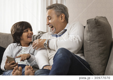 Smiling grandfather and grandson using mobile phone  30977070