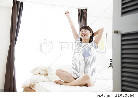 女性 目覚め 朝 起きる 伸び 寝室 ライフスタイル ベッドルームの写真素材