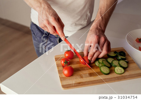 A man cutting food on a wooden board. 31034754